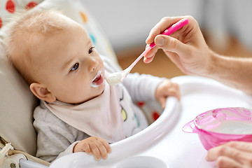 Image showing father feeding baby sitting in highchair at home