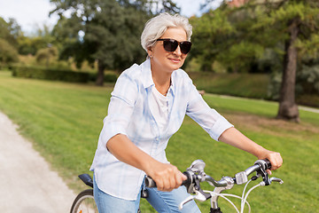 Image showing happy senior woman riding bicycle at summer park