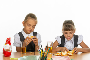 Image showing Two tired schoolgirls at recess eat an orange and drink juice