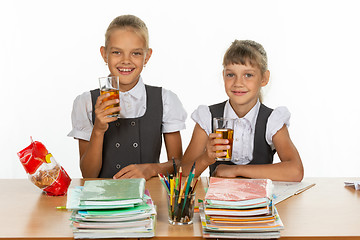 Image showing Two funny schoolgirls at a table drink juice, and look in the frame