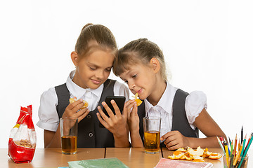 Image showing Two schoolgirls at a break look at the screen of a smartphone, and eat an orange and drink juice