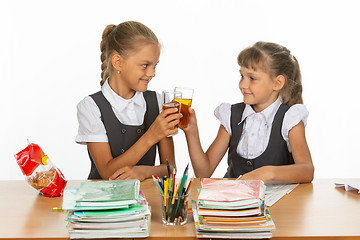 Image showing Two funny schoolgirls at a table drink juice, and banged glasses