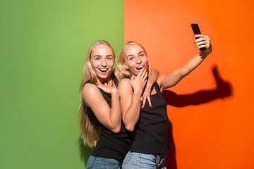 Image showing Portrait of a happy smiling casual girls making selfie photo by mobile phone isolated over studio background
