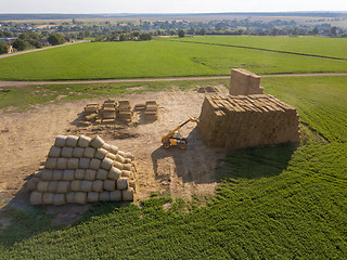 Image showing Green field with haystacks and agricultural machine around blue sky on an autumn sunny day.