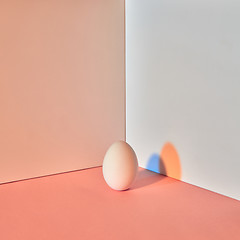 Image showing Colored egg with a reflection of blue-orange shadows around a double-beige-gray background with copy space. Easter concept.