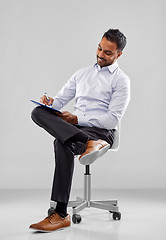 Image showing smiling indian businessman writing to clipboard