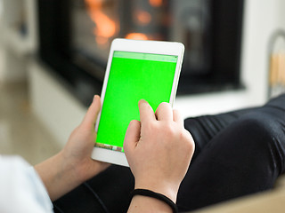 Image showing young woman using tablet computer in front of fireplace