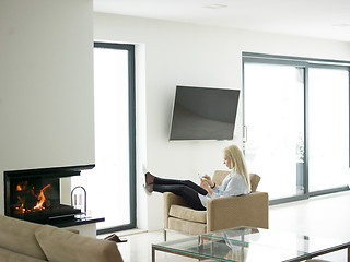 Image showing young woman using tablet computer in front of fireplace