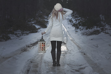 Image showing Woman walking along an icy road in winter with lantern