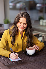 Image showing happy woman with notebook drinking cocoa at cafe