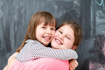 Image showing little girls hugging in front of chalkboard