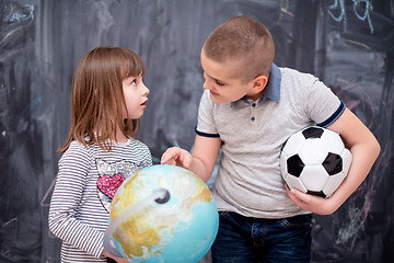 Image showing boy and little girl using globe of earth in front of chalkboard