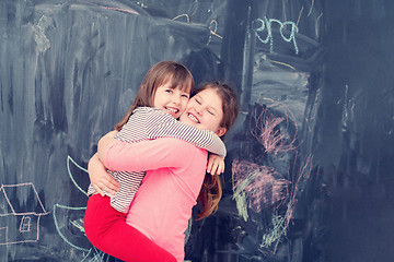 Image showing little girls hugging in front of chalkboard