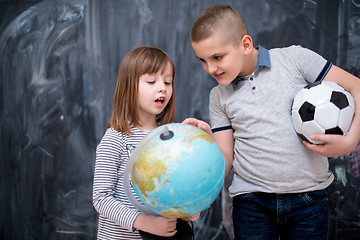 Image showing boy and little girl using globe of earth in front of chalkboard