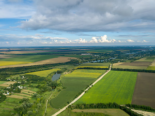 Image showing Panoramic view from drone to the countryside with a country buildings, dirt road and agricultural fields against cloudy sky in the summer at sunset.