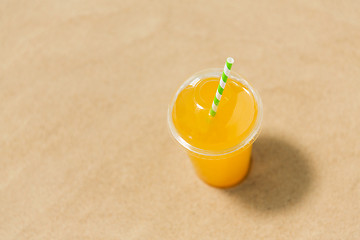 Image showing cup of orange juice with straw on beach sand