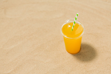 Image showing cup of orange juice with straw on beach sand