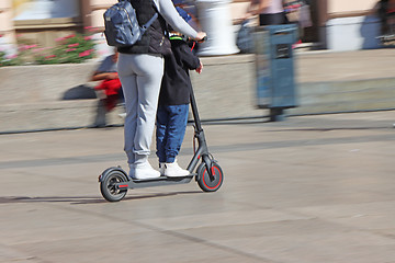 Image showing Mother and son riding electric kick scooter at the city square