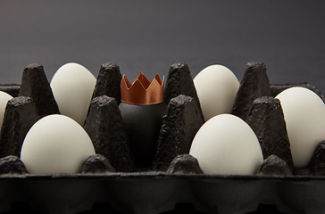 Image showing White and painted black egg decorated with a paper gold crown in a black cardboard box on a black background with space for text. Wealth concept