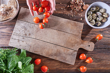 Image showing The hands of the woman put ripe tomatoes on a wooden board with quail eggs, pieces of nuts and copy space. The concept of cooking salad. Flat lay