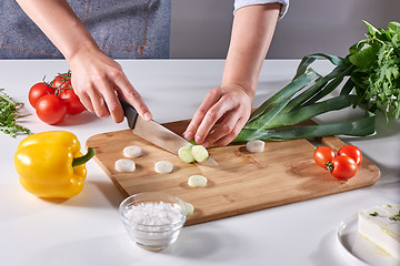 Image showing Fresh leek slices cut into the hands of a female cook on a wooden board on the kitchen table around a variety of organic vegetables. Cooking Healthy Salad