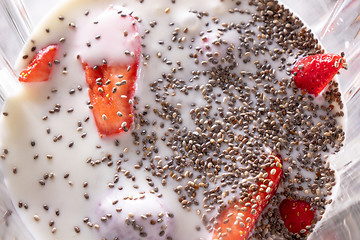 Image showing healthy fruits smoothies with shia seeds and strawberries in blender, close up. Flat lay