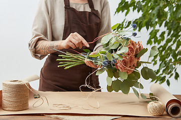 Image showing Female florist is decorating beautiful bouquet from fresh natural roses step by step at the table with paper and rope on it. Mother\'s Day holiday.