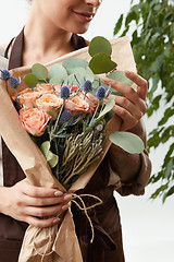 Image showing Close-up of greeting flowers bouquet of fresh natural roses living coral color in a florist girl\'s hands on a white background with green leaf.