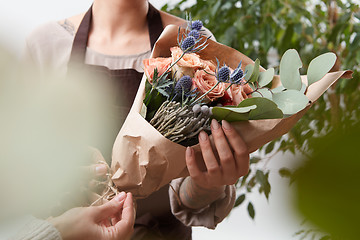 Image showing Close-up of roses flowers bouquet in a woman\'s hands on a blured green leaf background.