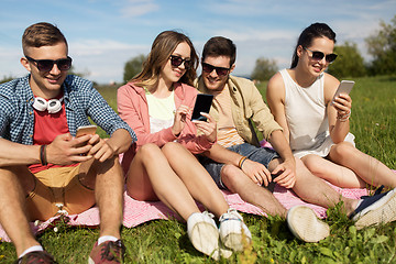 Image showing smiling friends with smartphones sitting on grass