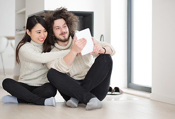 Image showing multiethnic couple using tablet computer in front of fireplace