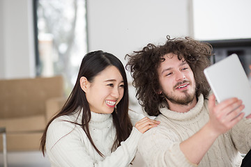 Image showing multiethnic couple using tablet computer in front of fireplace