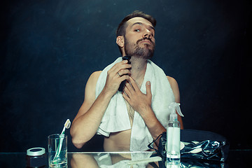 Image showing young man in bedroom sitting in front of the mirror scratching his beard