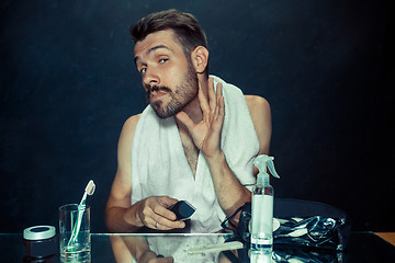 Image showing young man in bedroom sitting in front of the mirror scratching his beard