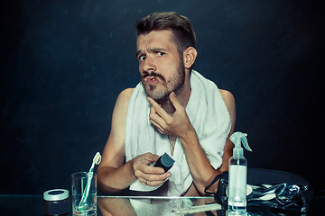 Image showing young man in bedroom sitting in front of the mirror scratching his beard