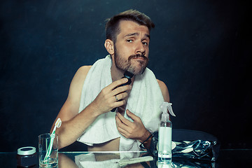 Image showing young man in bedroom sitting in front of the mirror scratching his beard