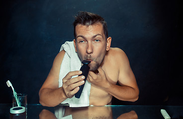 Image showing young man in bedroom sitting in front of the mirror scratching his beard