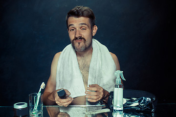 Image showing young man in bedroom sitting in front of the mirror scratching his beard