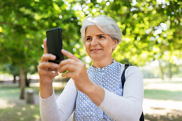 Image showing senior woman photographing by cell at summer park