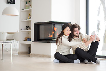 Image showing multiethnic couple using tablet computer in front of fireplace