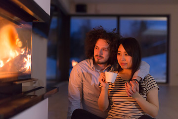 Image showing happy multiethnic couple sitting in front of fireplace