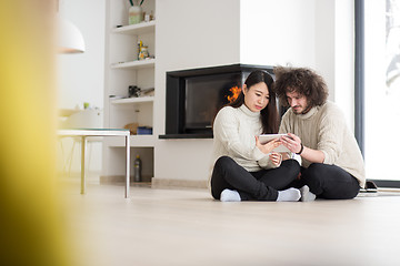 Image showing multiethnic couple using tablet computer in front of fireplace