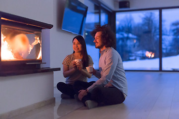 Image showing happy multiethnic couple sitting in front of fireplace