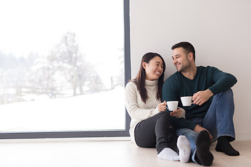 Image showing multiethnic couple enjoying morning coffee by the window