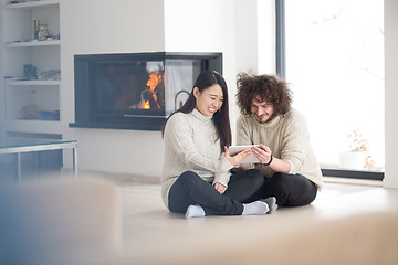 Image showing multiethnic couple using tablet computer in front of fireplace