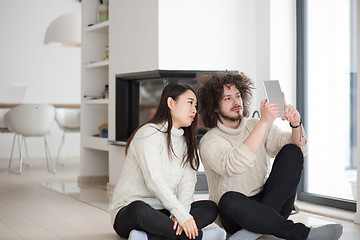 Image showing multiethnic couple using tablet computer in front of fireplace