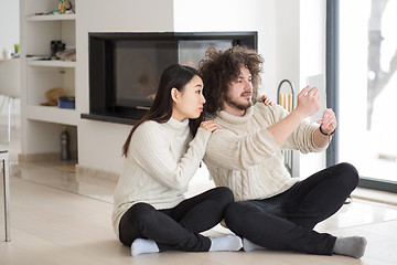 Image showing multiethnic couple using tablet computer in front of fireplace