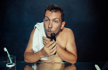 Image showing young man in bedroom sitting in front of the mirror scratching his beard