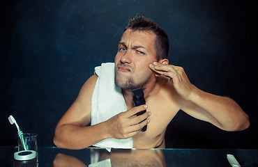 Image showing young man in bedroom sitting in front of the mirror scratching his beard