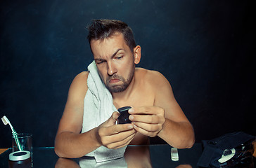 Image showing young man in bedroom sitting in front of the mirror scratching his beard